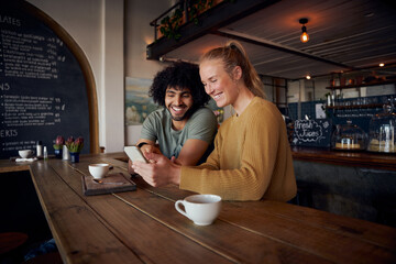 Smiling couple looking at smartphone sitting in modern cafe