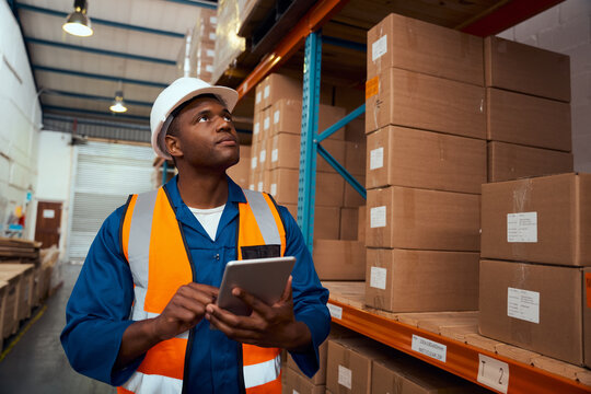 African male supervisor checking product or parcel goods on shelf pallet in industry storage warehouse using digital tablet