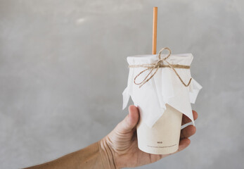 Woman hand is holding coffee cup with straw made from sugar product on gray background.