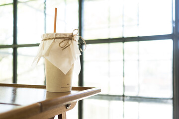 Paper coffee cup with straw made from sugar product on near window of cafe.