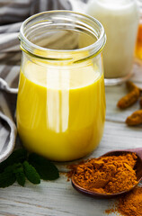 Yellow turmeric latte drink. Golden milk with cinnamon, turmeric, ginger  and honey over white wooden background.