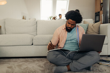 Afro man working at home at the cozy of the living room while using technology