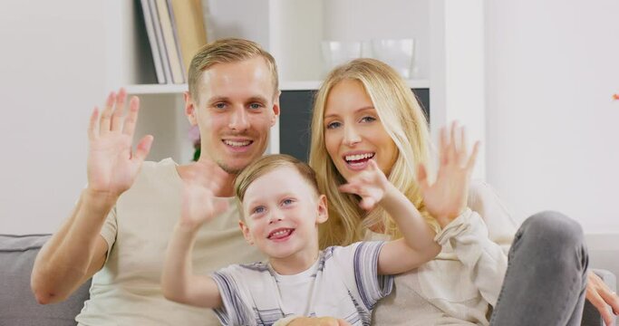 Happy parents sit on couch at home with cute little son wave talk on webcam, smiling young family with preschooler boy kid have conversation or shoot record vlog for social media together.