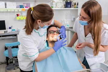 Obraz premium Female dentist with an assistant polishes teeth to a male patient in the dental clinic.