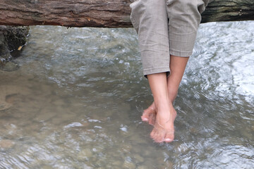 Legs of a woman in pants who sitting on a wood bridge and swinging her feet in a river