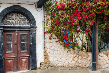 Antique oak door in an old stone house decorated with bright petunia flowers on a cloudy summer day