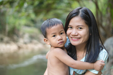 Asian mother in blue shirt with DIY chest pocket playing water with her son about 1 year and 9 months at  waterfall