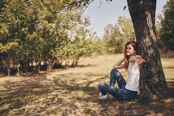 the traveler sits near a tree outdoors in the forest in jeans and a t-shirt