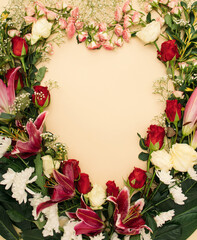 Fresh bloom floral, red, white and pink roses, white chrysanthemums and royal lilies on champagne background. heart-shaped frame. Minimal flat lay.