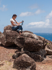 A woman sitting on a rock overlooking the ocean working on her laptop