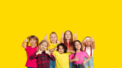Thumbs up. Portrait of little caucasian children gesturing isolated on yellow studio background with copyspace. Cheerful kid models. Concept of human emotions, facial expression, sales, ad, childhood.