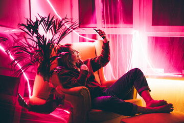  Young woman making video call with smart phone in living room with neon light at home .
