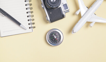 Old camera, notepad, toy airplane and compass on yellow background.