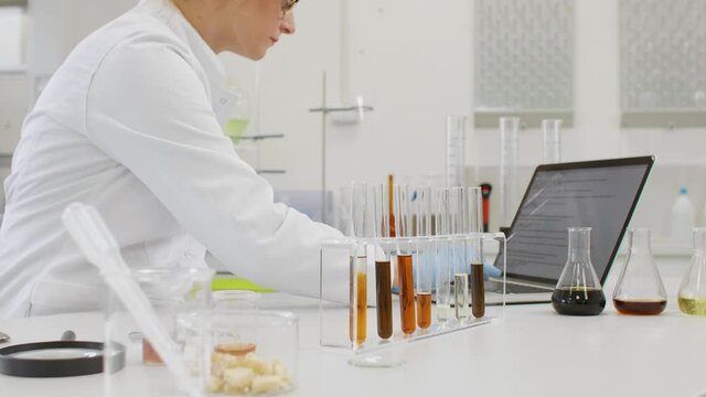 Chemist working with hemp CBD oil in laboratory and writing results in laptop.