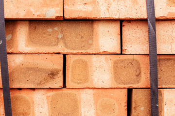 Red brick packed in stacks are stored on ground outdoors at a hardware store warehouse. Building...