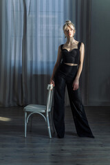 Naklejka premium Studio portrait of a pretty blonde woman in black top and black pants, looking to the side. Blue eyes, young and tender-2.