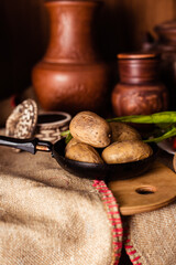 Boiled fresh potatoes in uniform on a wooden board in a cast-iron pan. Russian cuisine. Dinner in the Russian village. salt are on the table. On the background of clay pots