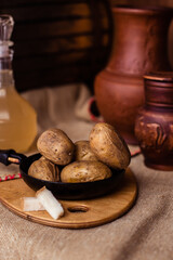 Boiled fresh potatoes in uniform on a wooden board in a cast-iron pan. Russian cuisine. Dinner in the Russian village. salt are on the table. On the background of clay pots