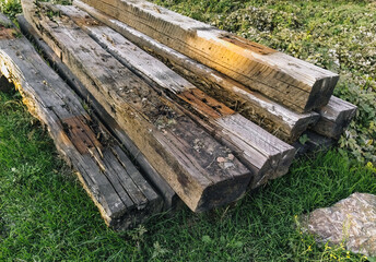 Old, used long wooden sleepers for railway repairs are scattered carelessly, lie on green grass for garbage, recycling. Preparatory work.