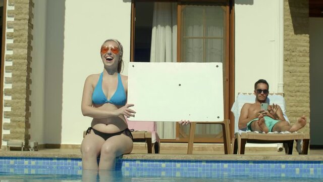 Smiling bikini woman holding a white billboard near the pool.Creative people can place whatever they want on the whiteboard.