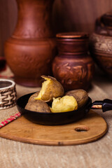 Boiled fresh potatoes in uniform on a wooden board in a cast-iron pan. Russian cuisine. Dinner in the Russian village. salt are on the table. On the background of clay pots