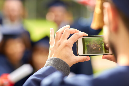 education, graduation, technology and people concept - group of happy international graduate students in mortar boards and bachelor gowns with diplomas taking picture with smartphone outdoors