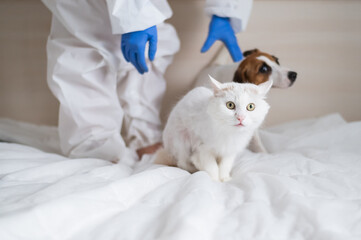 A woman in a protective suit is holding a dog and a cat