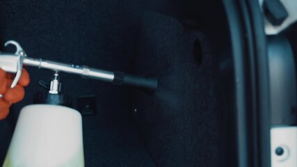 An employee of the car wash cleans the luggage compartment of the car interior. In his hands is a special tool - Powered by Adobe