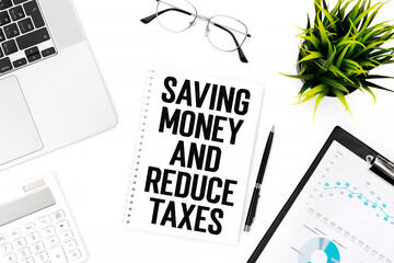 Text SAVING MONEY AND REDUCE TAXES on card on office desk with laptop, calculator, chart, clipboard, glasses, pen. Flat lay, top view.