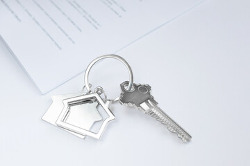 Close-up of a key with a keychain in the shape of a house, documents in the background. The concept of buying and insuring real estate, apartments, mortgages. Light colors, copy space.
