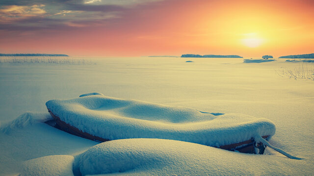 Winter sunset landscape with lonely snow covered boat
