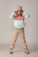 Beautiful little girl in a striped sweater, light pants and a knitted hat