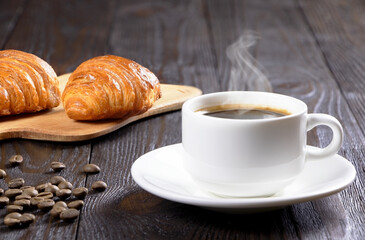 A cup of hot coffee and croissants on a wooden background. Breakfast with coffee and fresh pastry. Copy space. Fresh cake and pastry