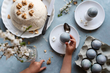 Easter table with traditional food and little hands of child with easter eggs and paschal cake. Retro style on dining table with tasty breakfast. Close up and top view. 