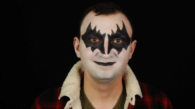 Man in demon makeup looking and camera and smiling on black background