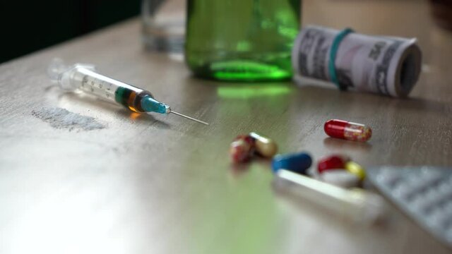 syringe with heroin cocaine and pills standing on the table after a party. bad habits and drug addiction concept