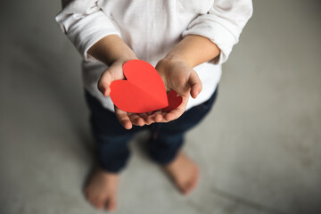 Two baby hands holding red paper hearts.
