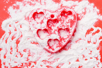 On a red background, a silicone mold in the shape of a heart and scattered flour. St.Valentine's day concept.