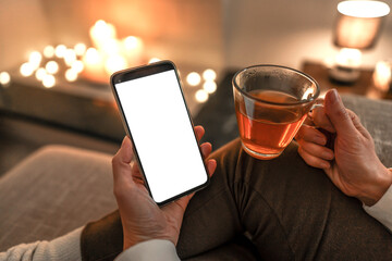 New reading technology using smartphone to enjoying preferred ebook: close up of unrecognizable woman sitting on sofa holding cup of tea in one hand and big display cell phone with blank white screen