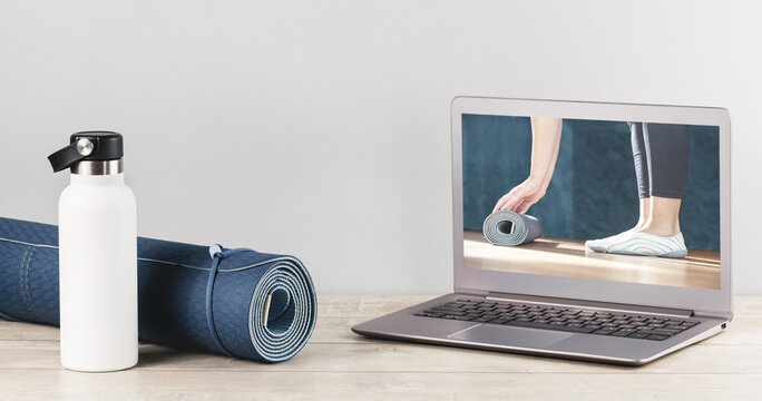 Yoga mat with water flask and with online yoga class video on laptop screen. Practicing pilates and fitness at home during lockdown and quarantine. Remote sessions. banner copy space