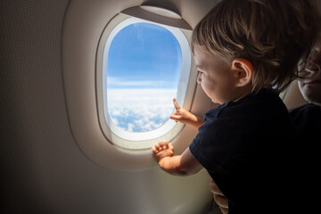 Fototapeta na wymiar cute toddler points his finger at the sky through the window. first flight concept, traveling with children.