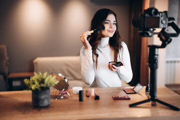 Beauty blogger pretty female filming daily make-up routine tutorial on camera. Influencer young woman live streaming cosmetics product review in home studio. Vlogger job. DIY putting makeup