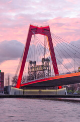 Obraz premium Rotterdam, The Netherlands, January 13, 2021: monumental railway bridge De Hf seen through one of the pylons of Willems Bridge against a dramatic sky at sunrise