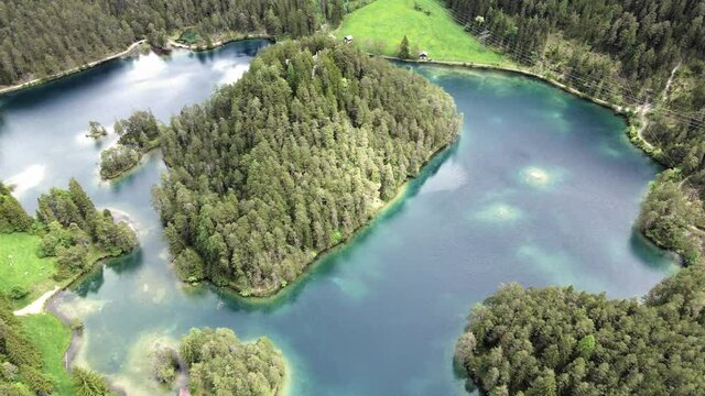 ein alpen see mit einer bewaldeten insel umgeben von blau t&uuml;rkisen wasser von oben betrachtet