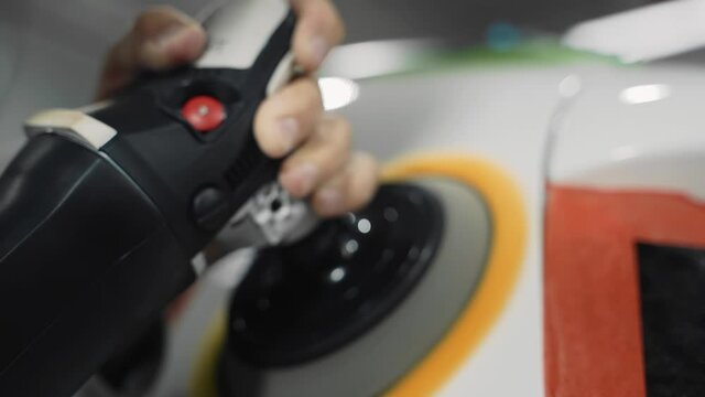 A guy with a tool in his hands polishes the surface of the car body in a car dealership. Taken in close-up