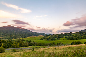 Landscape of grassed hills with the road serpentine ot the foreground and expressive soft clouds on the sky at dusk