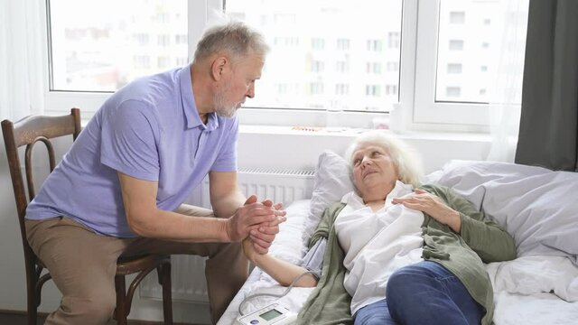 caring elderly man checks his wife's blood pressure with hypertension while lying at home in bed, health care.