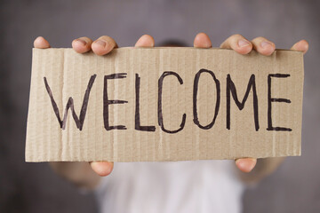 piece of paper with the word Welcome in hand on a gray background