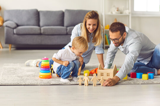 Young parents play with their son wooden figurines sitting on the floor among various toys. Mother, father and child spend time at home in a cozy children's room. Family holiday concept.