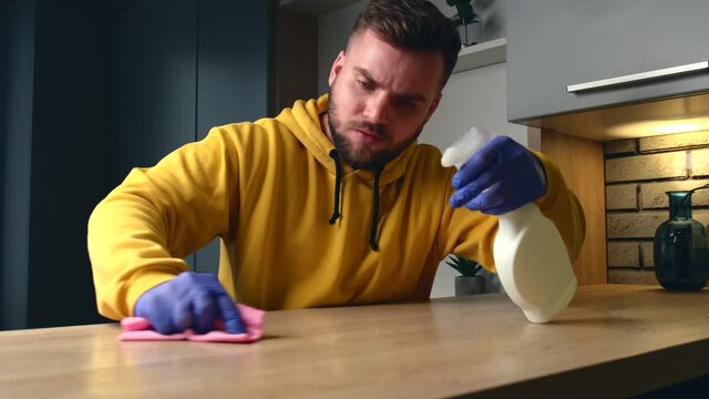 caucasian man wearing gloves and yellow sweater is cleaning and sanitizing the house with spray